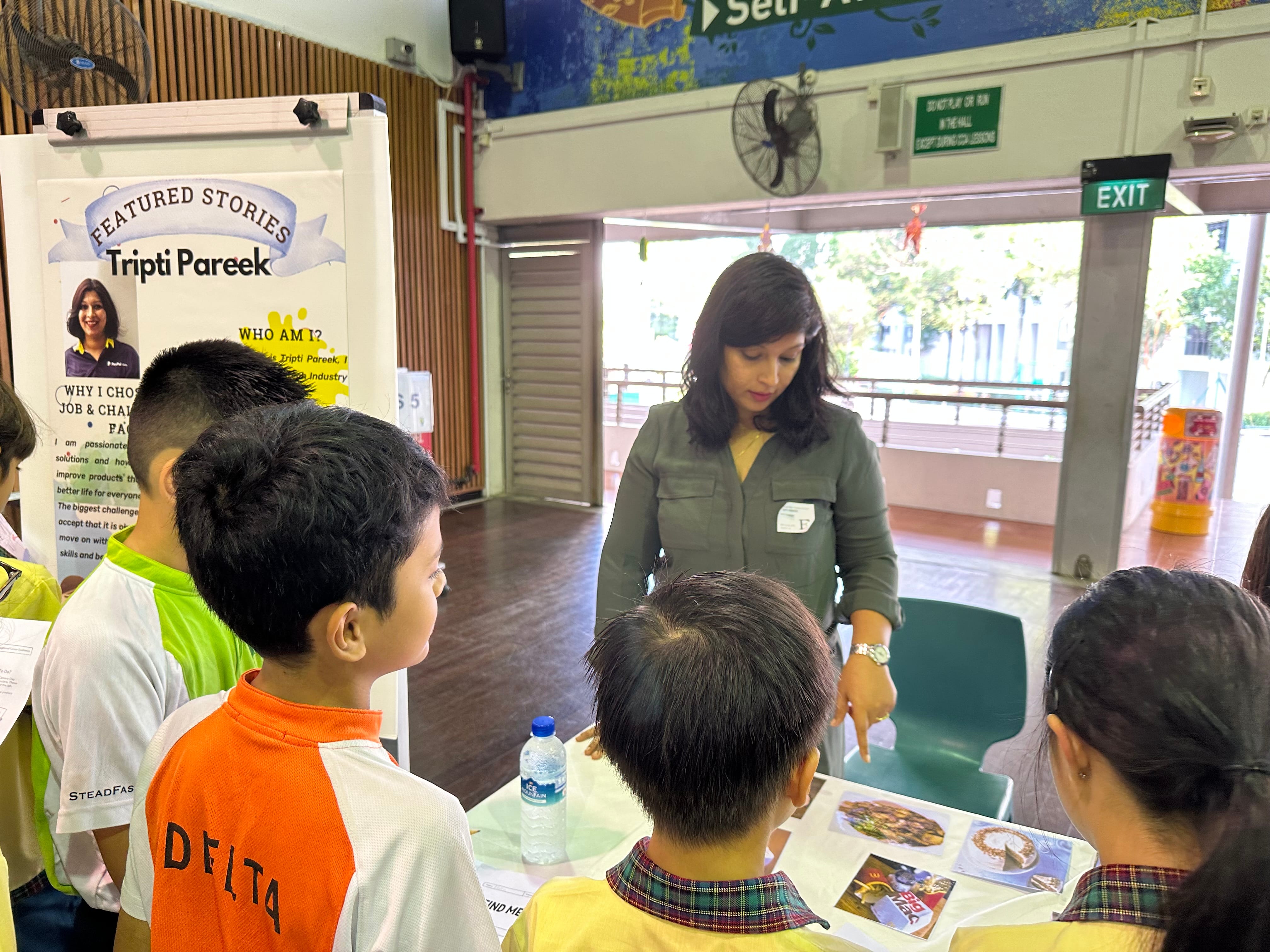 A woman named Tripti Pareek speaks to a group of children at a Featured Stories booth in a school hall.